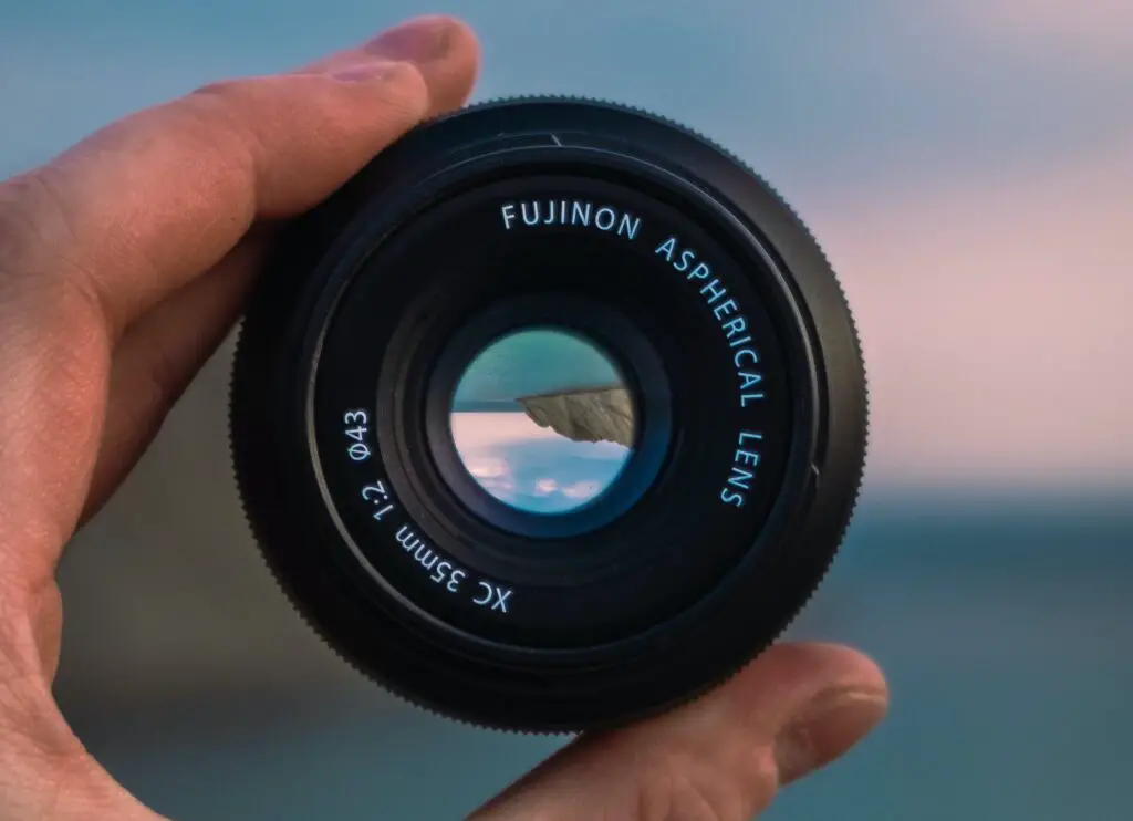 A 35mm lens being held with a blur landscape background