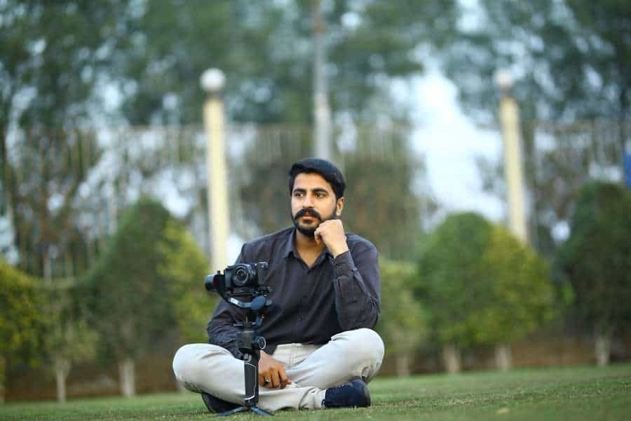 Man sitting on the grass with a camera attached to a gimbal in front of him
